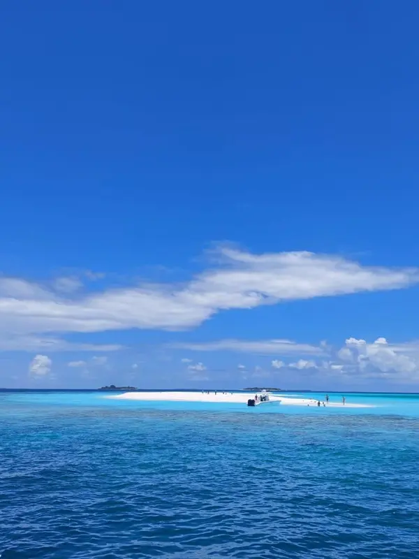 Un banc de sable blanc émerge d'une eau turquoise sous un ciel bleu nuageux.