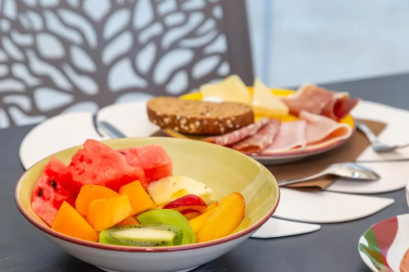 Une table est dressée avec des fruits, de la charcuterie et du pain.