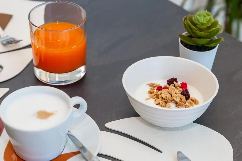 Petit déjeuner avec un jus d'orange, un café et un bol de yaourt aux fruits.