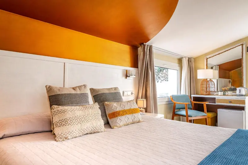 Une chambre lumineuse avec un grand lit décoré de coussins et un coin bureau.