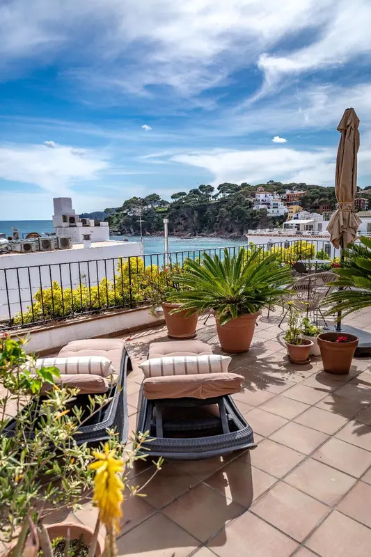 Transats et plantes ornent une terrasse ensoleillée avec vue sur la mer.