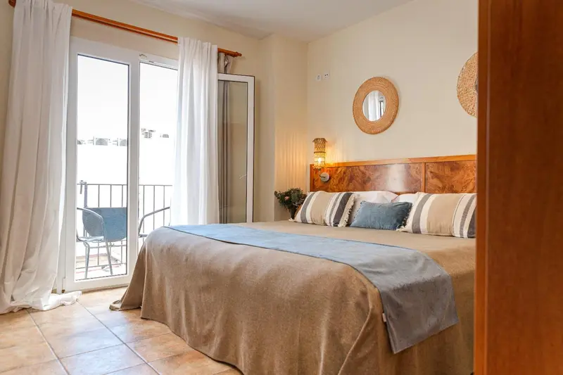 Une chambre lumineuse avec un grand lit et un accès à un balcon.