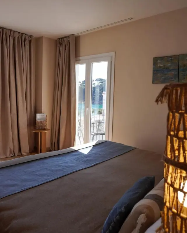 Une chambre lumineuse avec un lit et une vue sur la mer par de grandes baies vitrées.