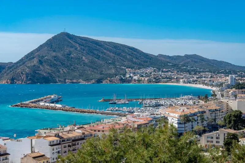 Vue aérienne d'une ville côtière avec une montagne en arrière-plan et un port de plaisance.