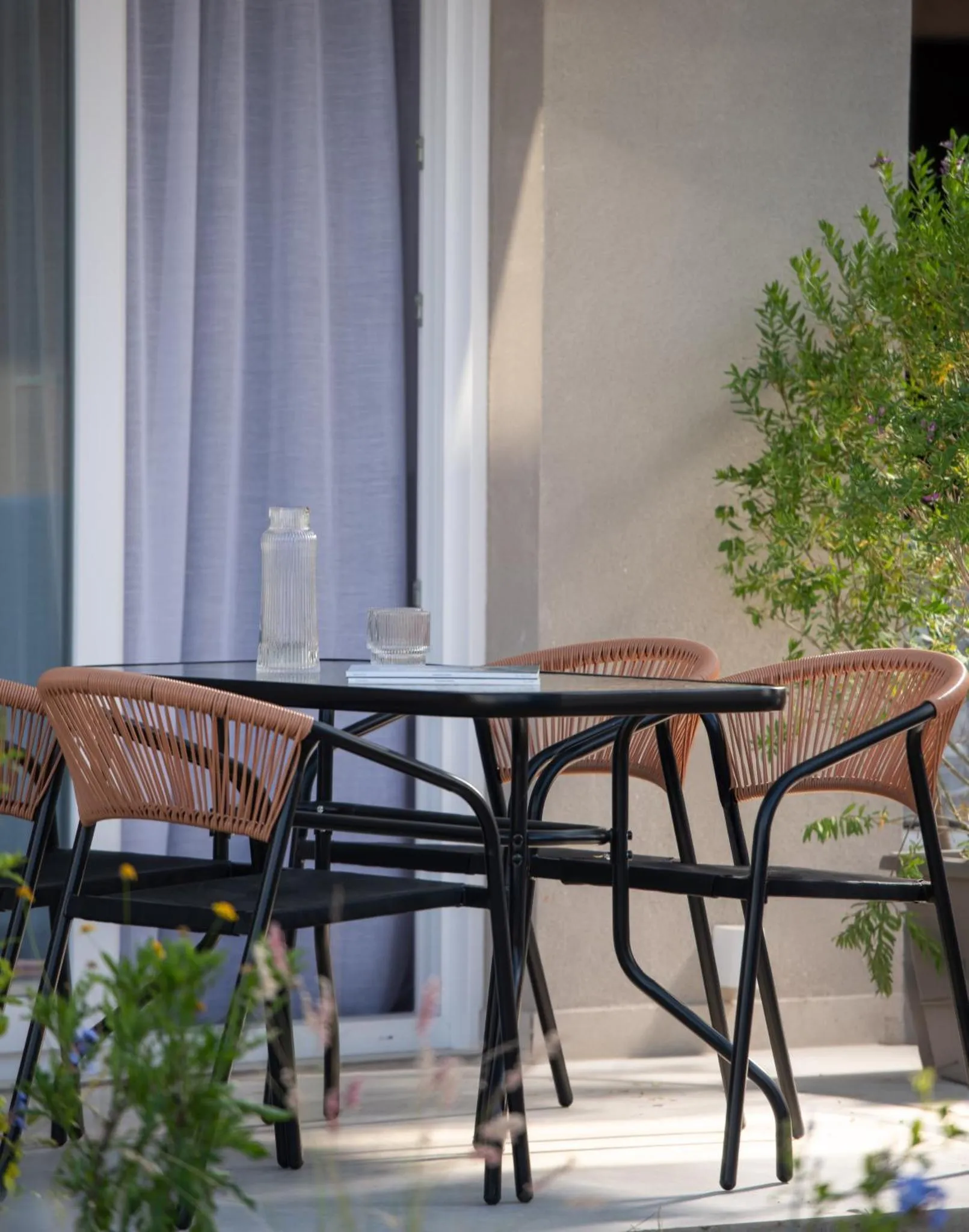 Une table ronde en métal avec des chaises en osier sur une terrasse ombragée.