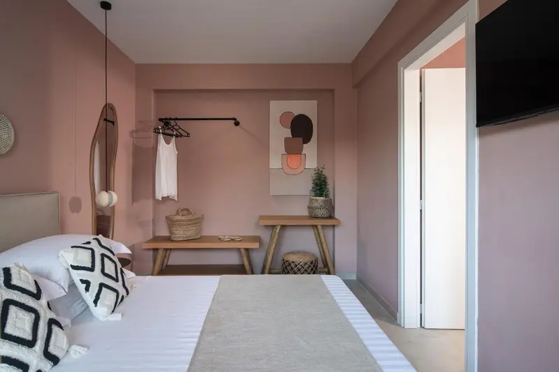Une chambre aux murs roses avec un lit recouvert d'une courtepointe blanche et un tableau décoratif.