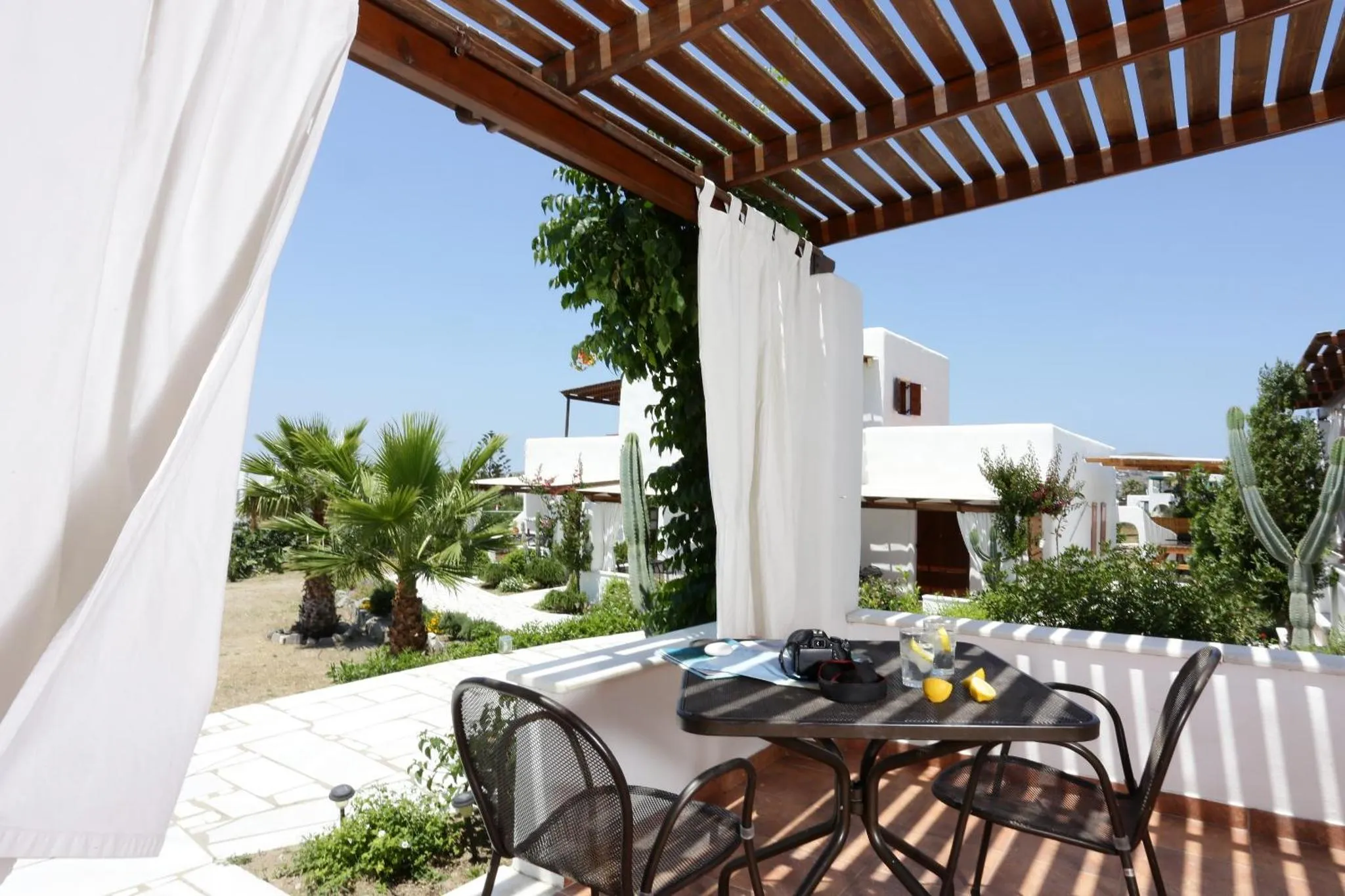 Une table et des chaises se trouvent sur une terrasse ombragée avec vue sur un jardin.