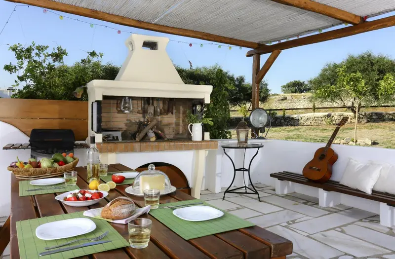 Une table est dressée pour un repas en extérieur, près d'un barbecue et d'une zone de détente.