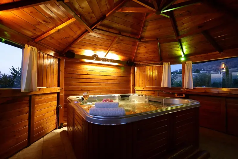Un jacuzzi extérieur en bois avec des serviettes enroulées et un verre de vin sur le bord.