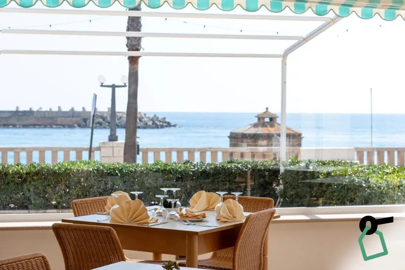 Une table est dressée avec de la vaisselle et des couverts devant une vue sur la mer.