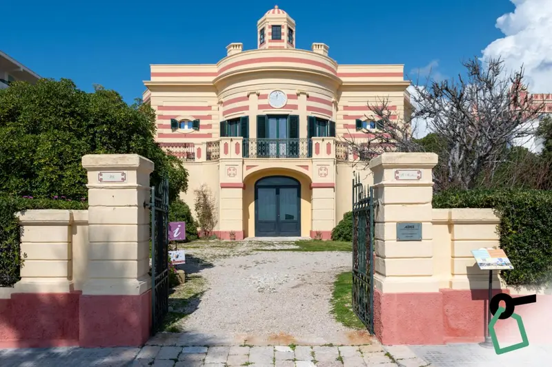Façade d'un bâtiment jaune et blanc avec une entrée monumentale et un jardin.