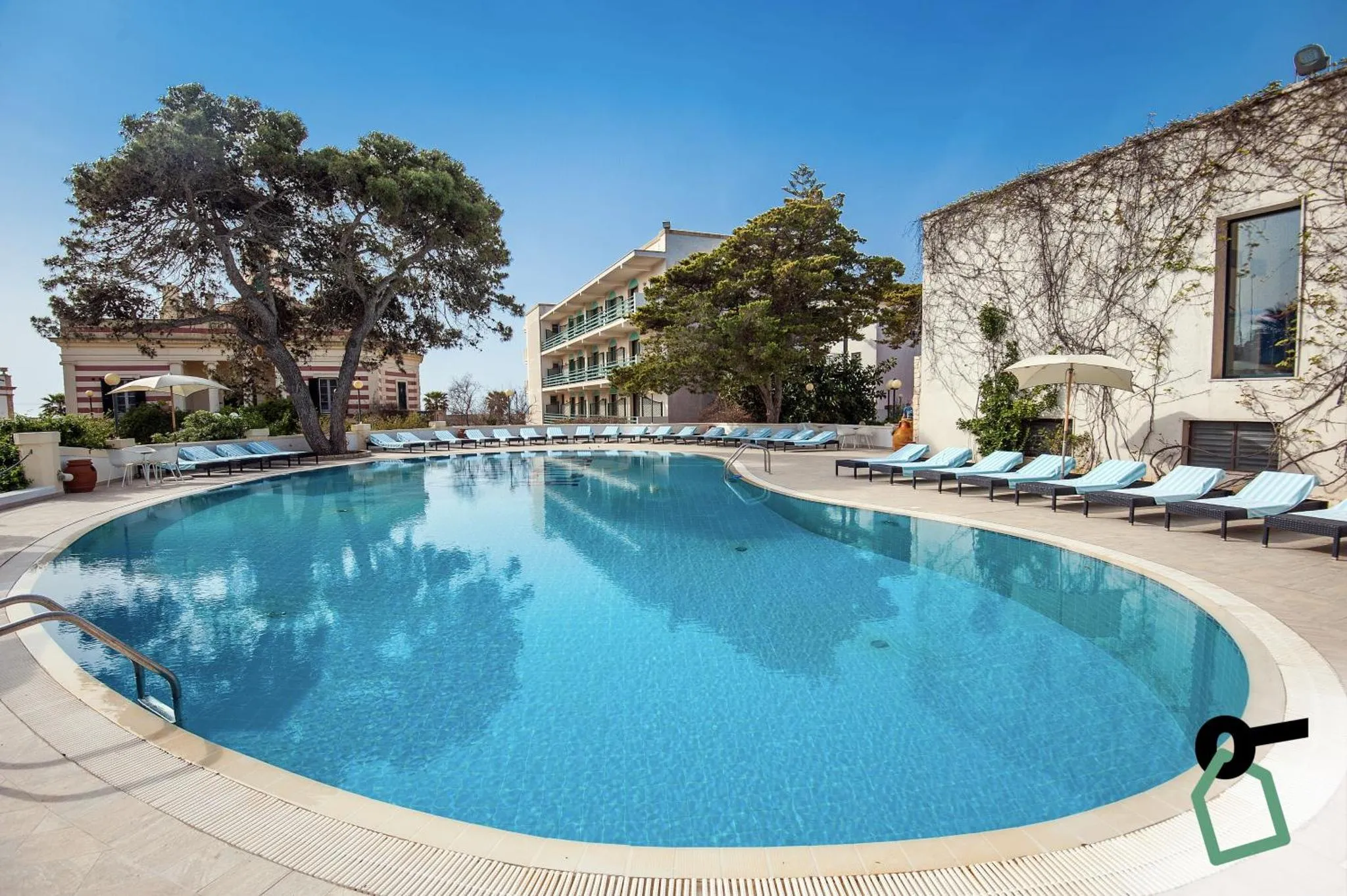 Une piscine rectangulaire bordée de transats sous un ciel bleu.