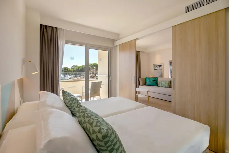 Une chambre lumineuse avec un lit double et un espace salon ouvert sur un balcon.