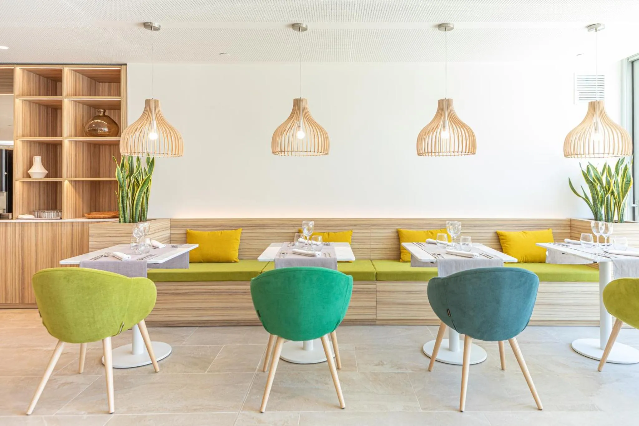 Une salle lumineuse avec des tables dressées et des banquettes colorées.