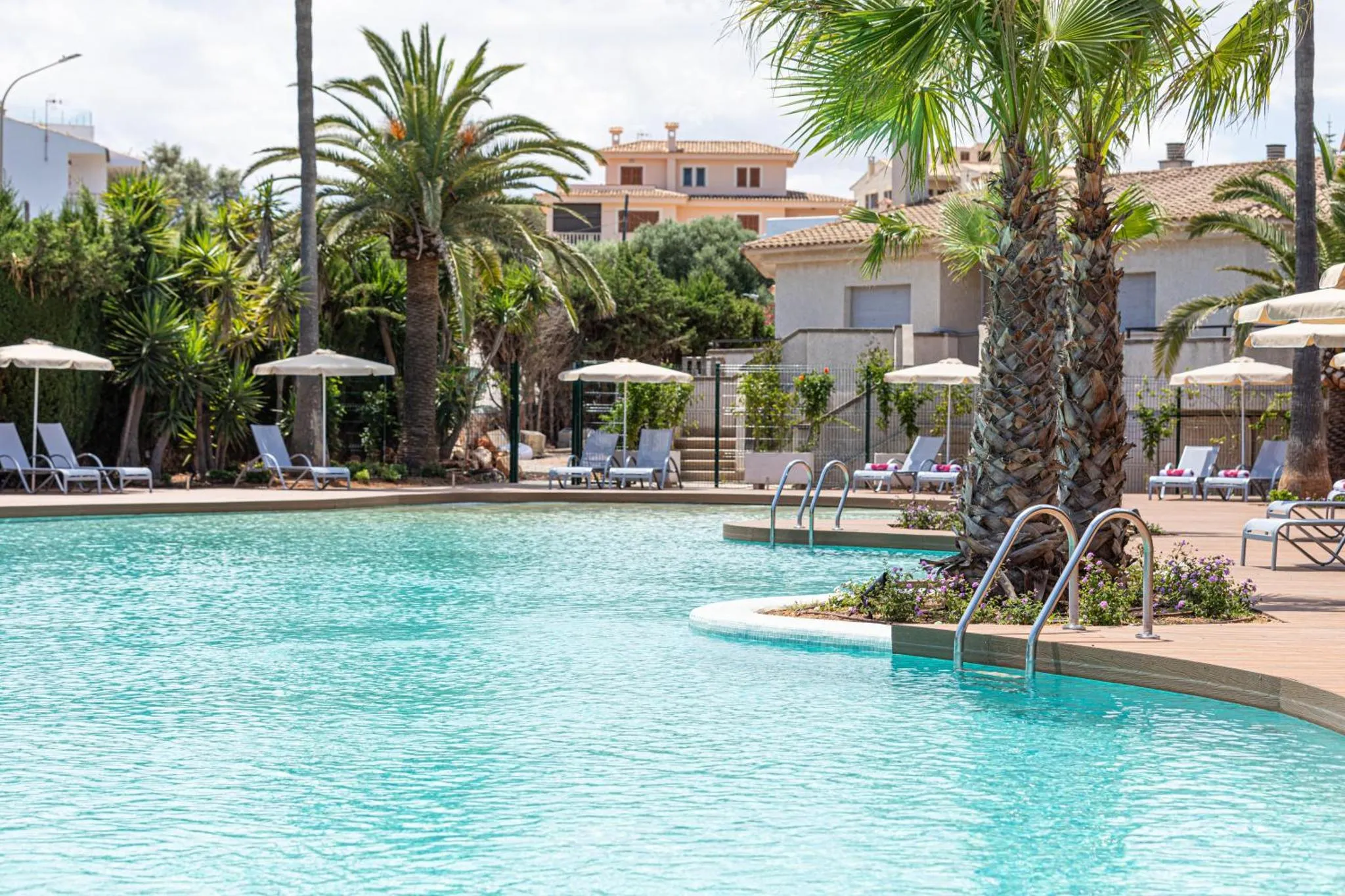 Une piscine turquoise bordée de transats et de palmiers sous le soleil.