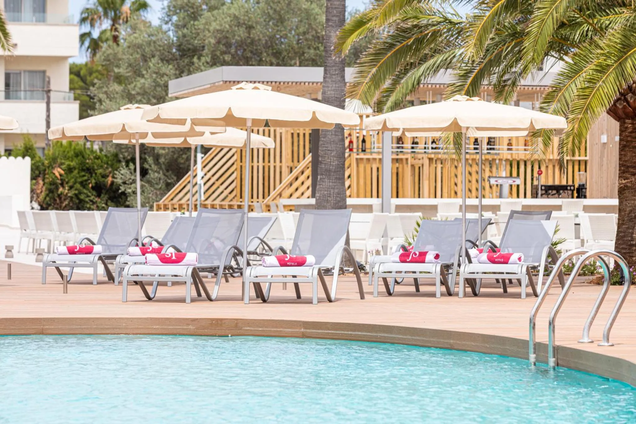 Transats et parasols bordent une piscine turquoise sous les palmiers.