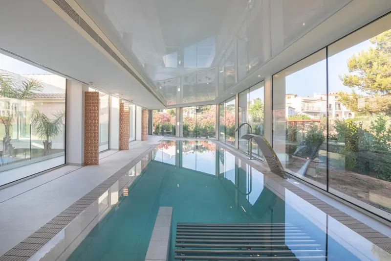 Une piscine intérieure lumineuse avec de grandes baies vitrées donnant sur un jardin.