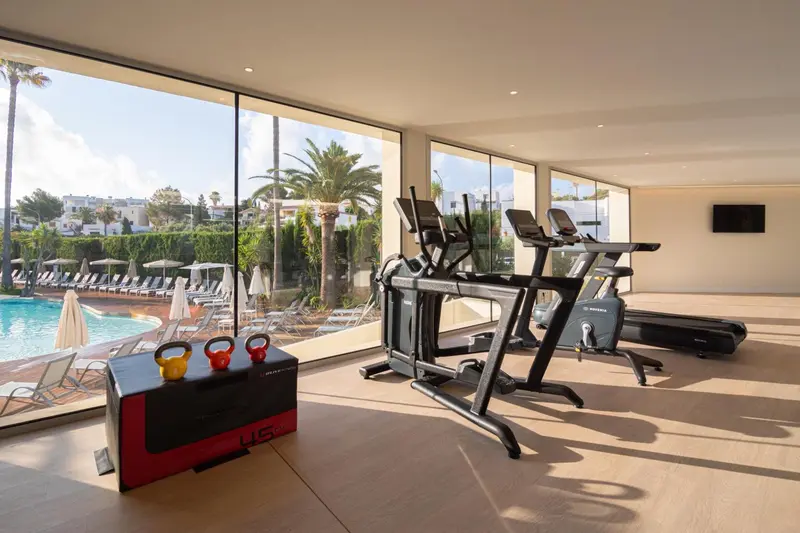 Une salle de sport lumineuse donne sur une piscine et une végétation tropicale.