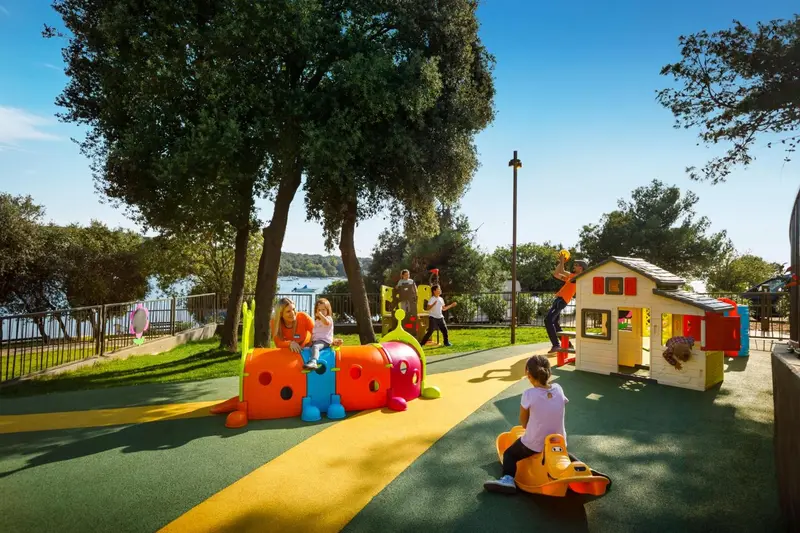Des enfants jouent sur une aire de jeux colorée avec des structures en plastique et un sol amortissant.