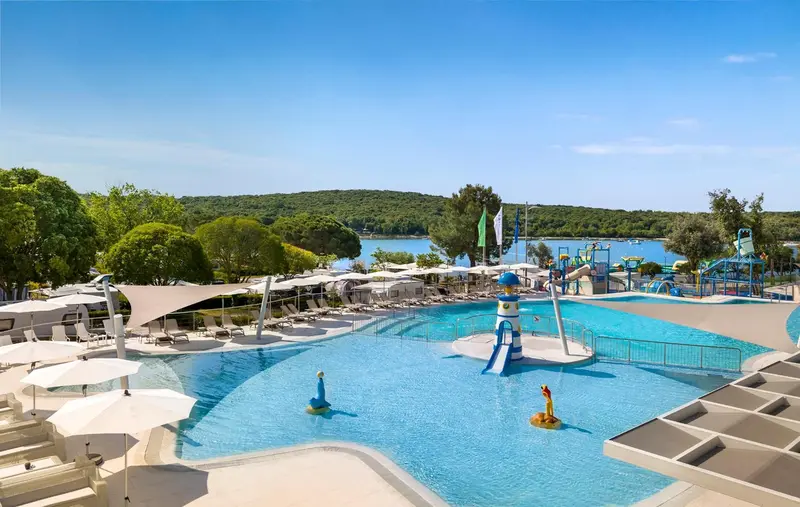 Piscine extérieure avec toboggans et transats sous des parasols.