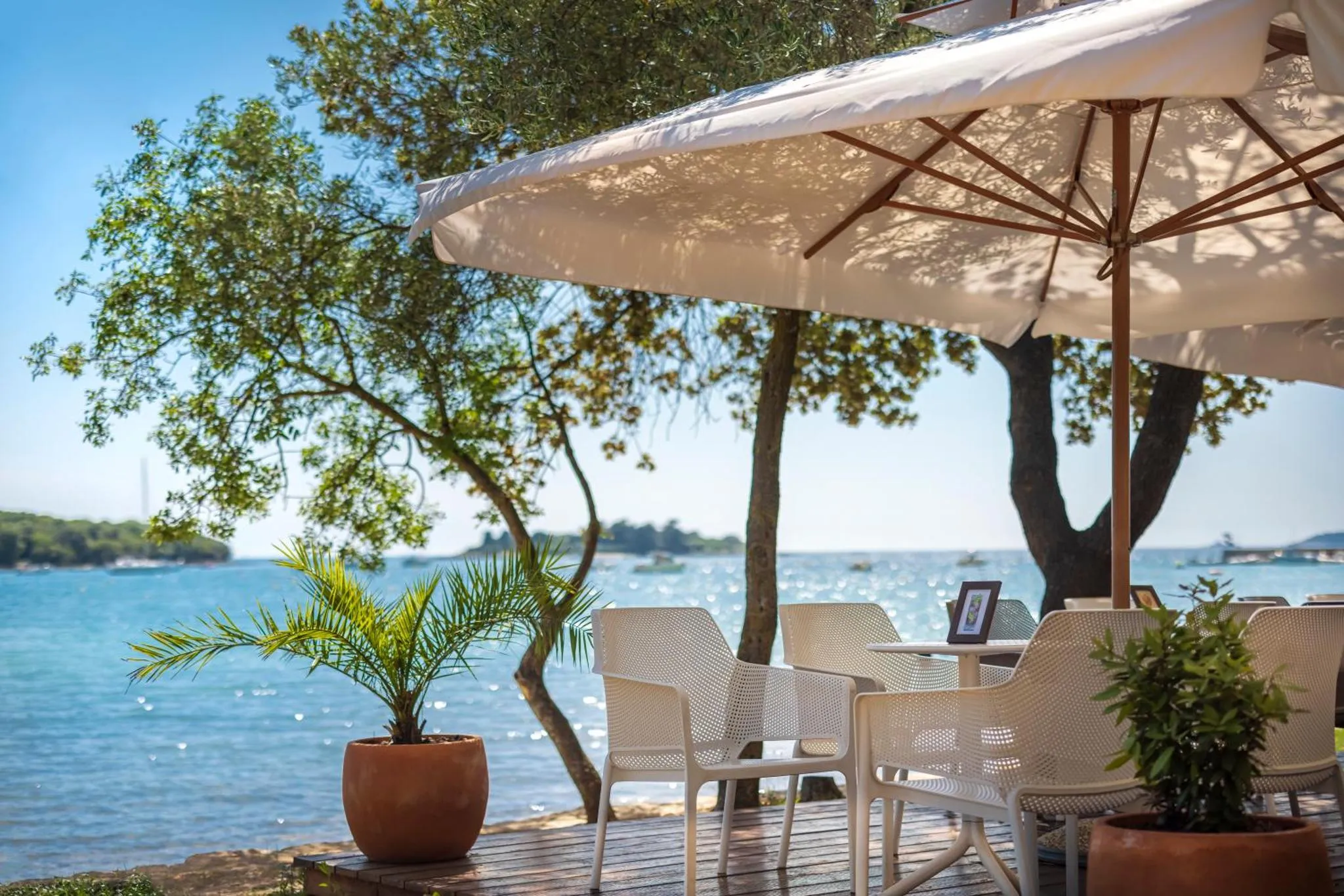 Terrasse ombragée avec mobilier en plastique blanc face à la mer.