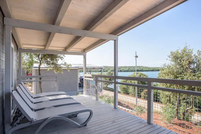 Terrasse en bois avec transats blancs donnant sur un paysage côtier.