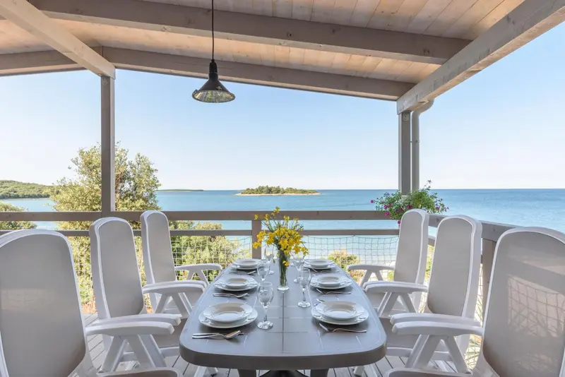 Table de repas dressée sur une terrasse avec vue sur la mer et un îlot.