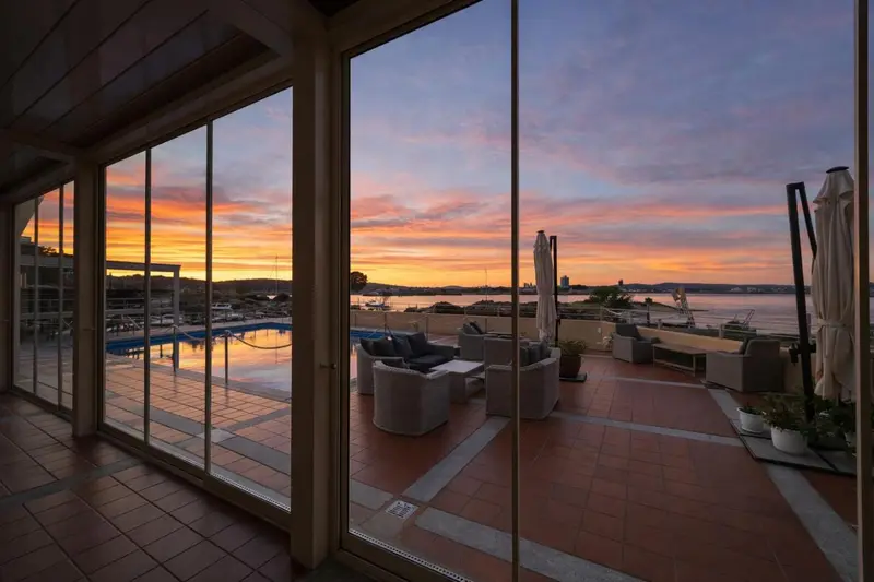 Terrasse avec mobilier d'extérieur donnant sur une piscine et une vue sur la mer au coucher du soleil.