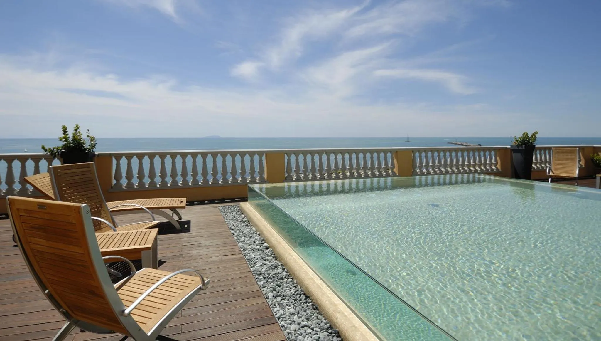 Transats et piscine à débordement sur une terrasse ensoleillée avec vue sur la mer.