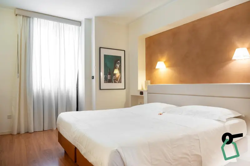 Une chambre lumineuse avec un grand lit recouvert d'une couette blanche.