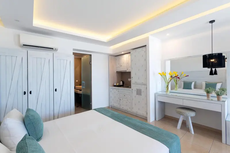 Une chambre lumineuse avec un lit fait et un coin cuisine.