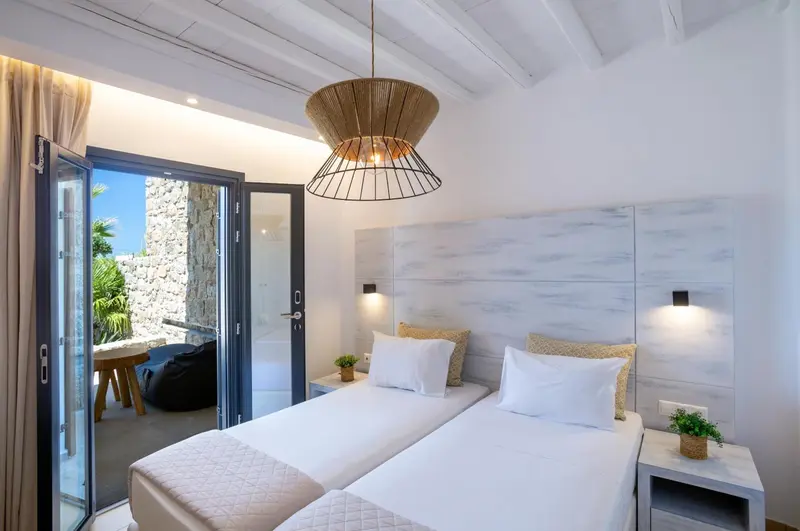 Chambre lumineuse avec deux lits simples et accès à une terrasse.