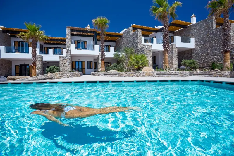 Une piscine turquoise bordée de palmiers et de bâtiments blancs.