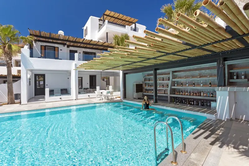 Une piscine turquoise bordée d'une terrasse ombragée et d'un bar.