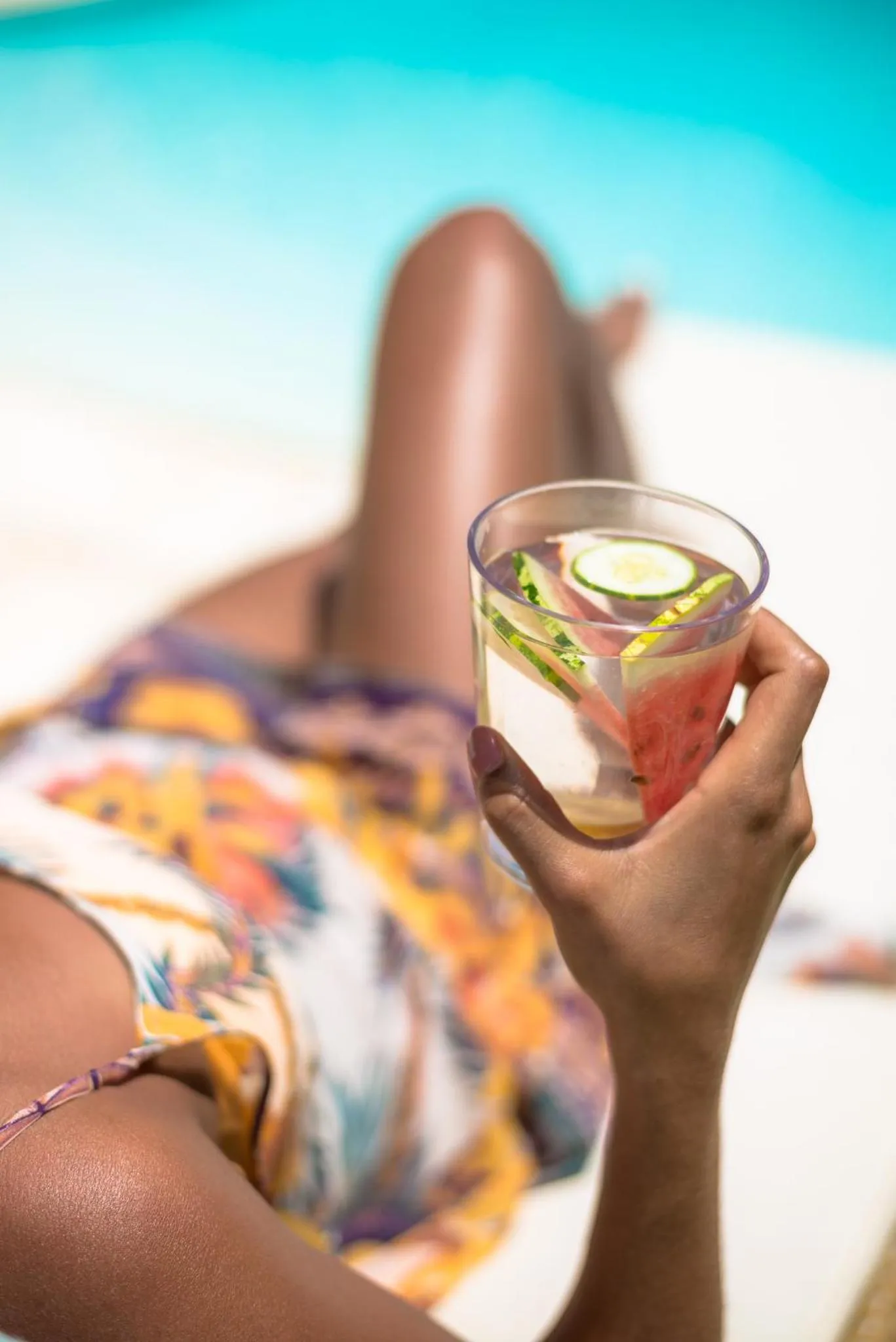 Une personne se relaxe au bord d'une piscine avec une boisson fraîche.