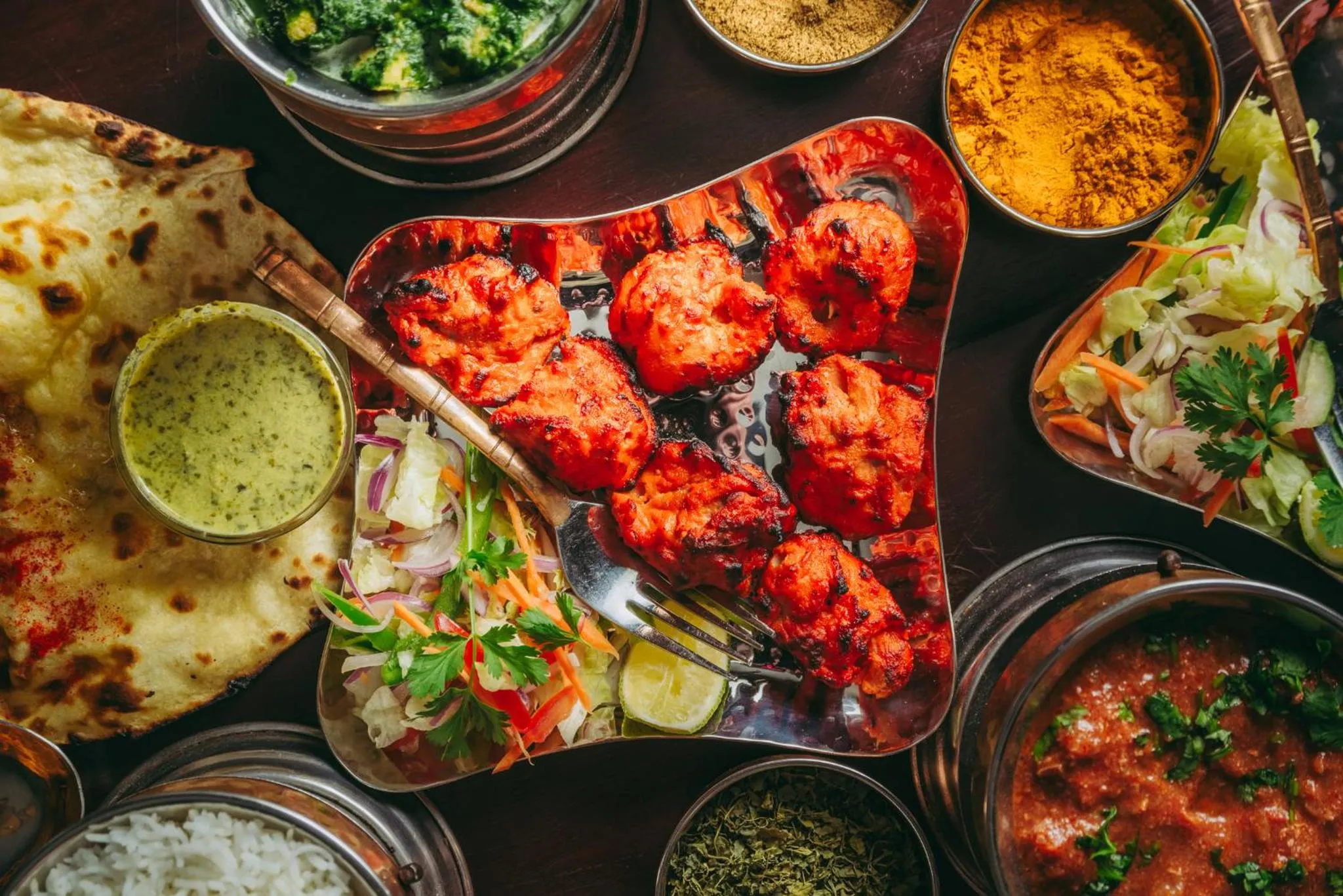Assortiment de plats indiens colorés servis sur une table en bois.