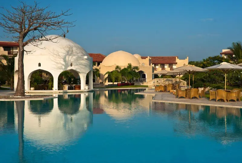 Une piscine turquoise reflète un bâtiment blanc et des parasols.