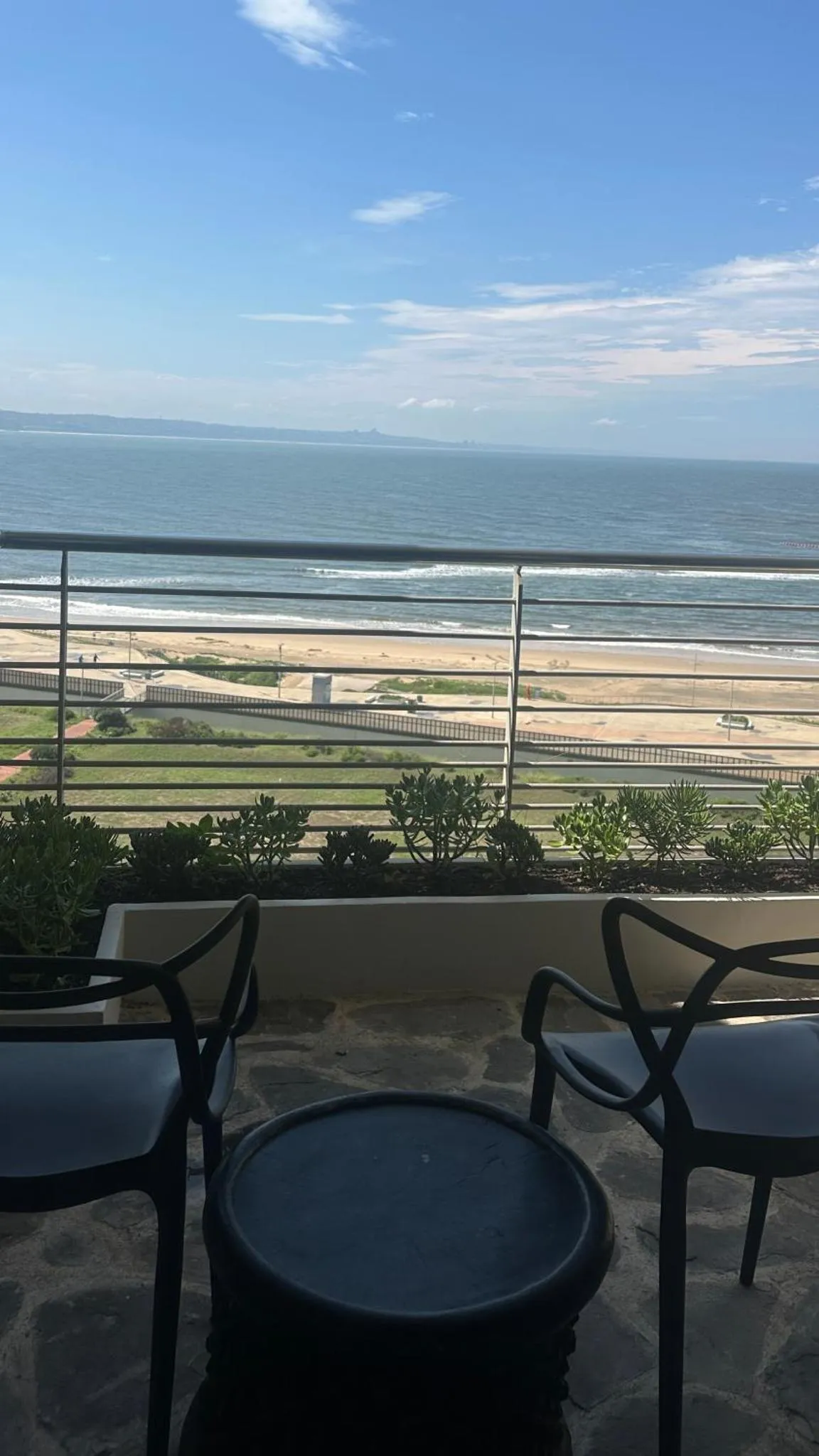 Vue d'une terrasse avec mobilier noir donnant sur une plage et la mer.