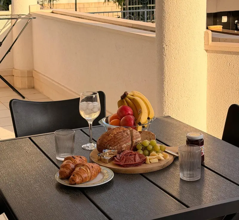 Une table en bois présente un petit-déjeuner avec des viennoiseries, des fruits et des boissons.