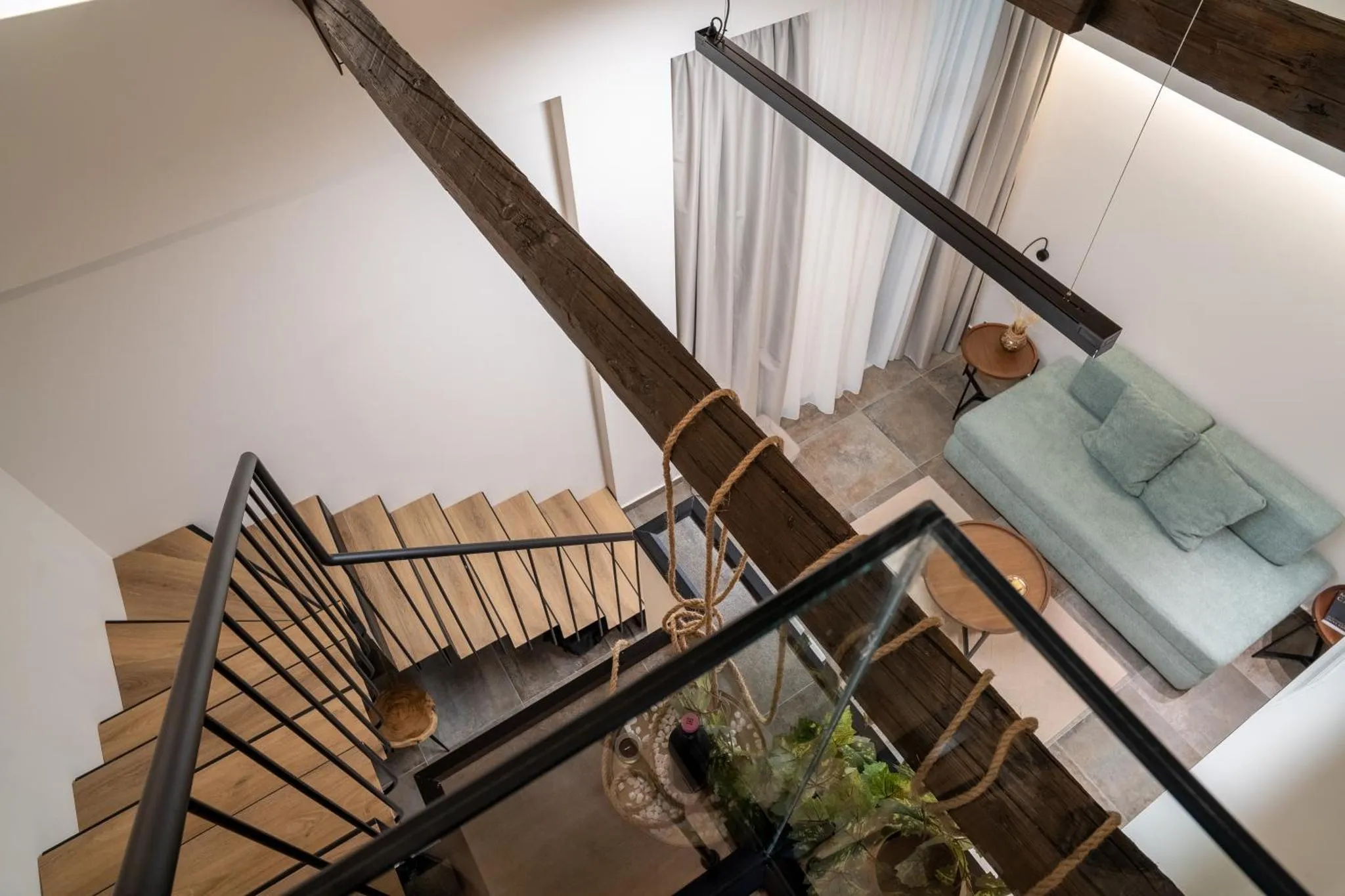 Vue d'un escalier en bois sombre descendant vers un espace salon avec canapé bleu.