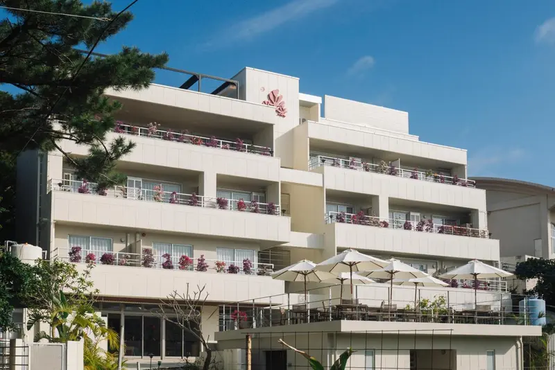 Bâtiment blanc à plusieurs étages avec des balcons fleuris et des parasols.