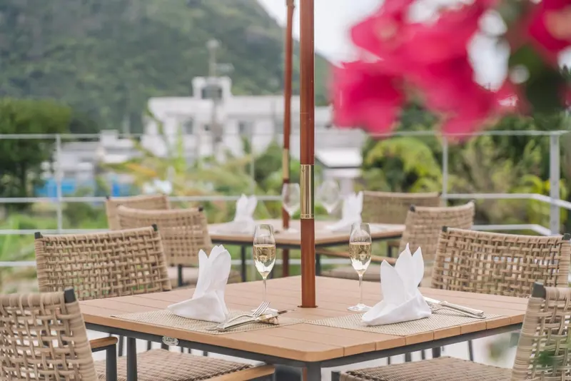 Une table est dressée avec des couverts et des verres sur une terrasse ensoleillée.