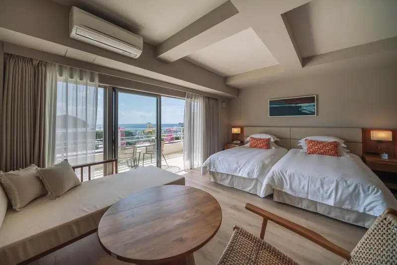 Chambre lumineuse avec deux lits simples et vue sur la mer.