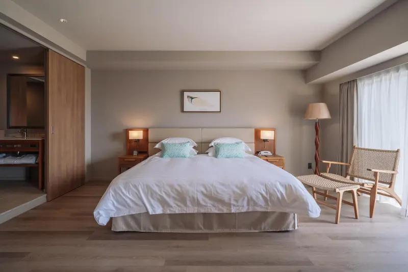 Une chambre lumineuse avec un grand lit et un fauteuil en bois.