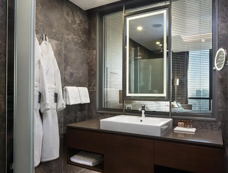 Une salle de bain moderne avec un grand miroir éclairé et des peignoirs blancs.