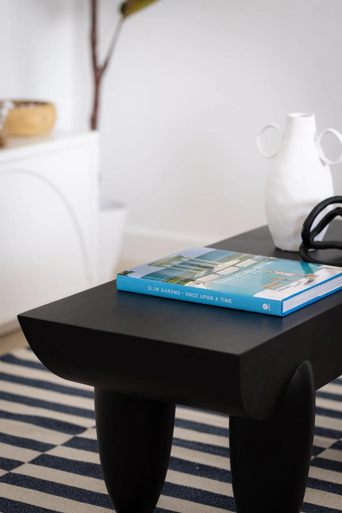 Une table basse sombre supporte un livre ouvert sur un tapis rayé.