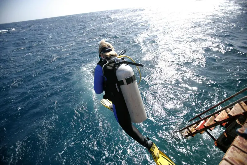 Une personne équipée de matériel de plongée se prépare à entrer dans l'eau depuis un bateau.
