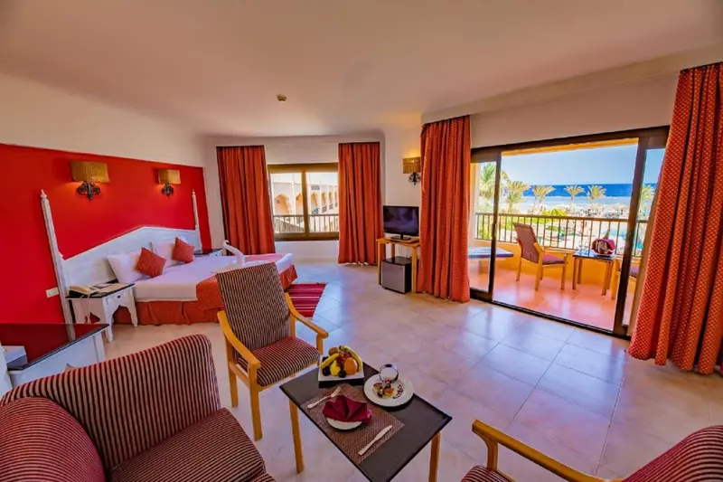 Une chambre lumineuse avec un lit double et un coin salon donnant sur une terrasse.