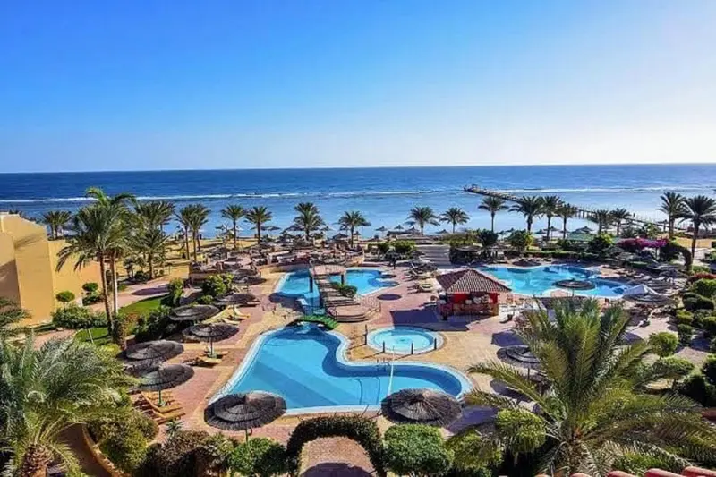 Vue aérienne d'un complexe hôtelier avec plusieurs piscines et la mer en arrière-plan.