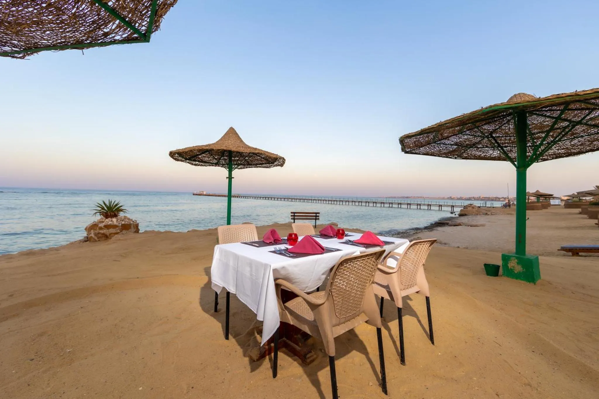 Table dressée sur une plage de sable fin, avec parasols en chaume et vue sur la mer.